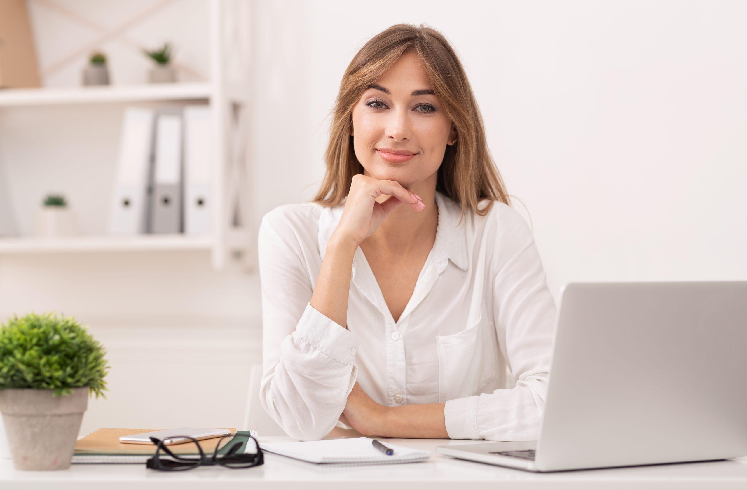 Management. Positive Business Lady Sitting At Laptop Touching Chin Looking At Camera In Modern Office.